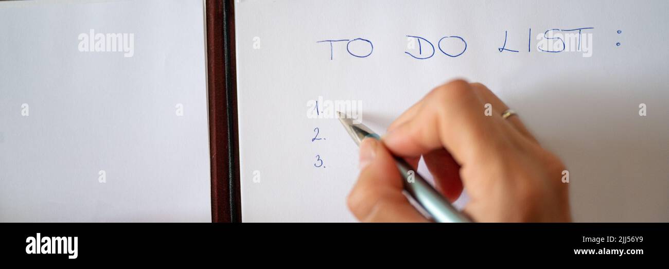 Immagine grandangolare della mano femminile che scrive una lista di cose da fare su un foglio bianco di carta. Vista dall'alto. Foto Stock