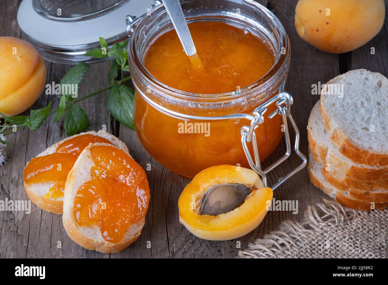 Marmellata di albicocche in un vaso di vetro e pane su un vecchio tavolo di legno Foto Stock