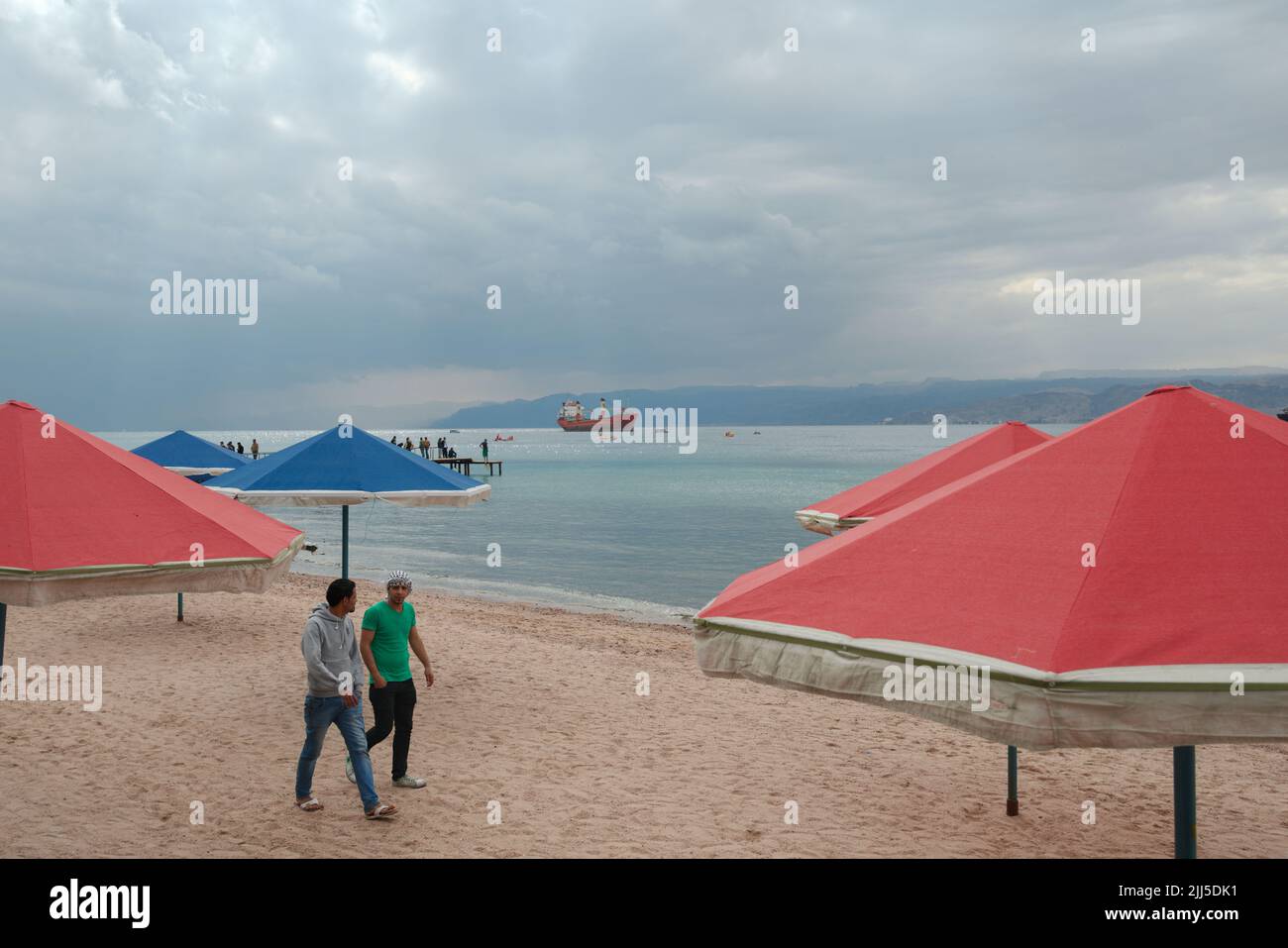 Uomini locali sulla spiaggia di Aquaba, Giordania tra ombrelloni Foto Stock