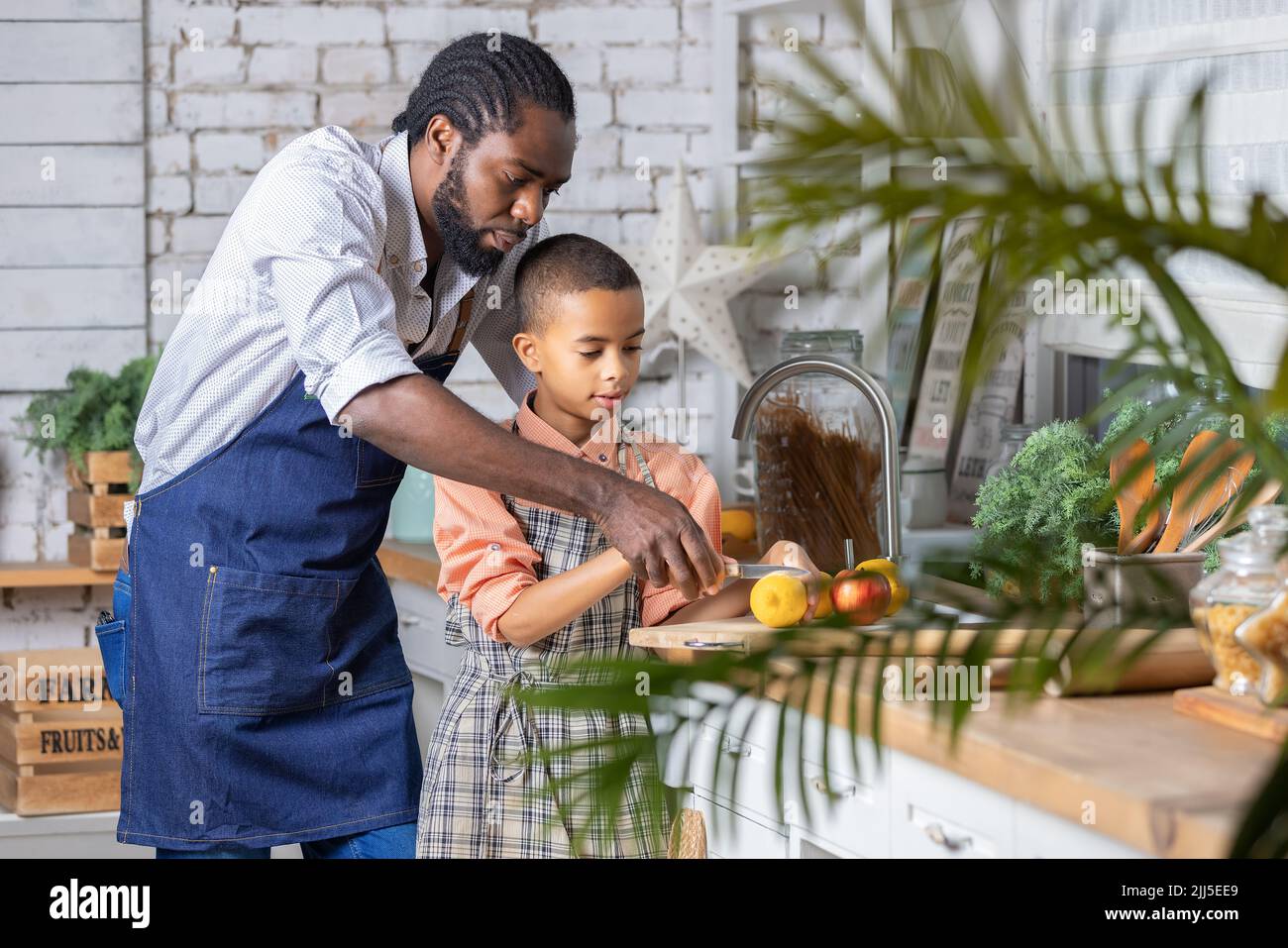 Il padre nero e il bambino che cucinano verdure fresche in cucina a casa. Papà africano e bambino ragazzo che si preparano insieme. Foto Stock