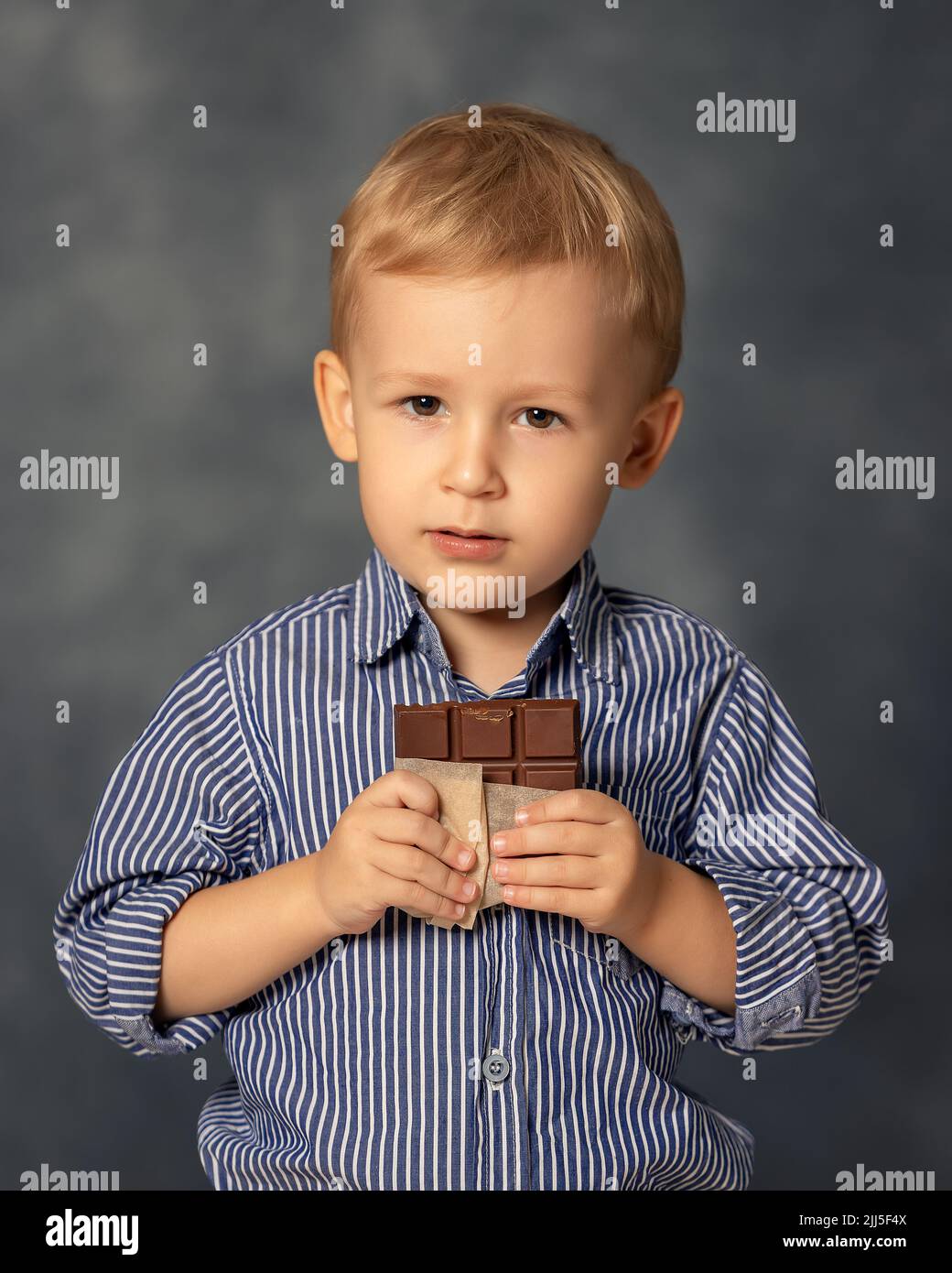 Ritratto di bambino piccolo che mangia cioccolato su sfondo grigio.  Concetto di infanzia felice. Dente dolce Foto stock - Alamy
