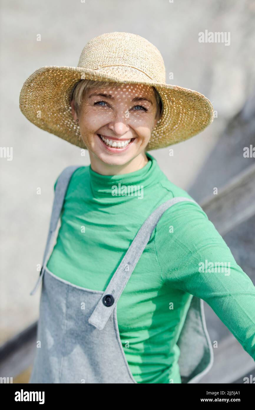 Donna felice che indossa il cappello in piedi in giorno di sole Foto Stock