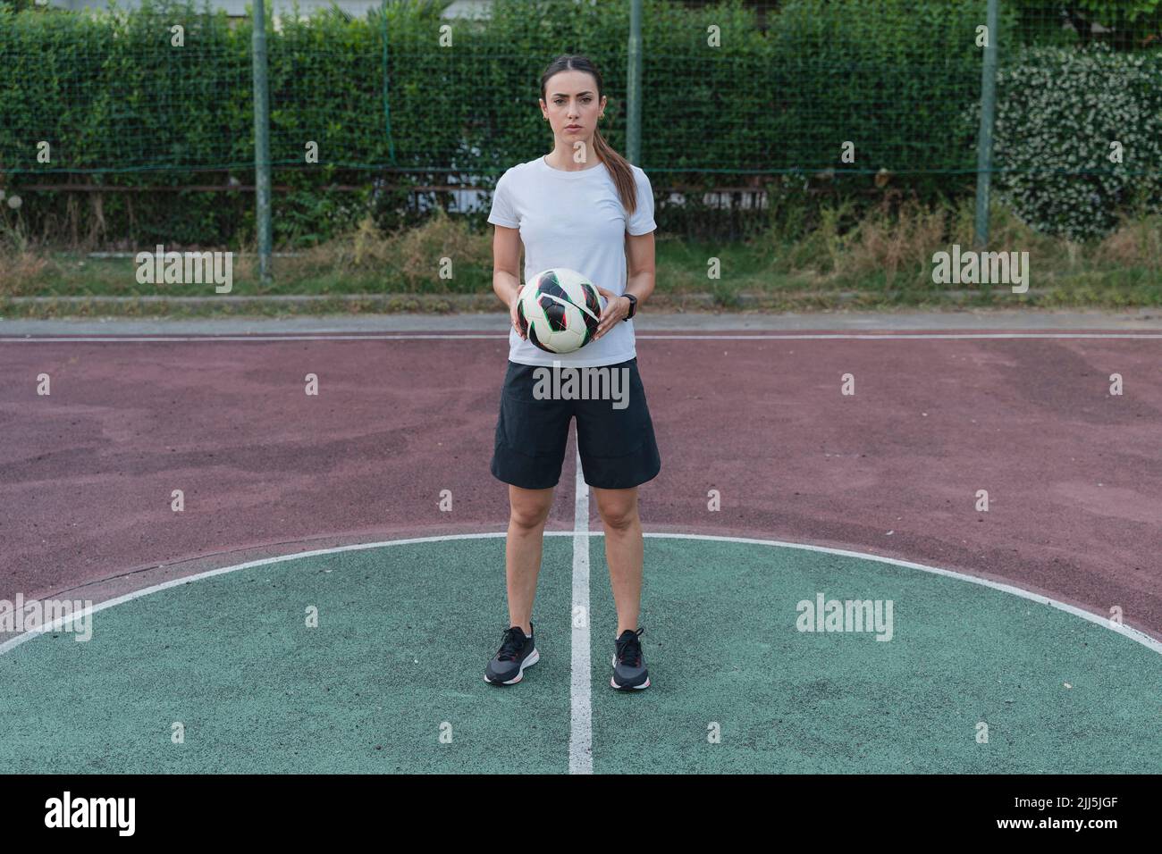 Giovane donna che tiene la palla in piedi in campo di calcio Foto Stock