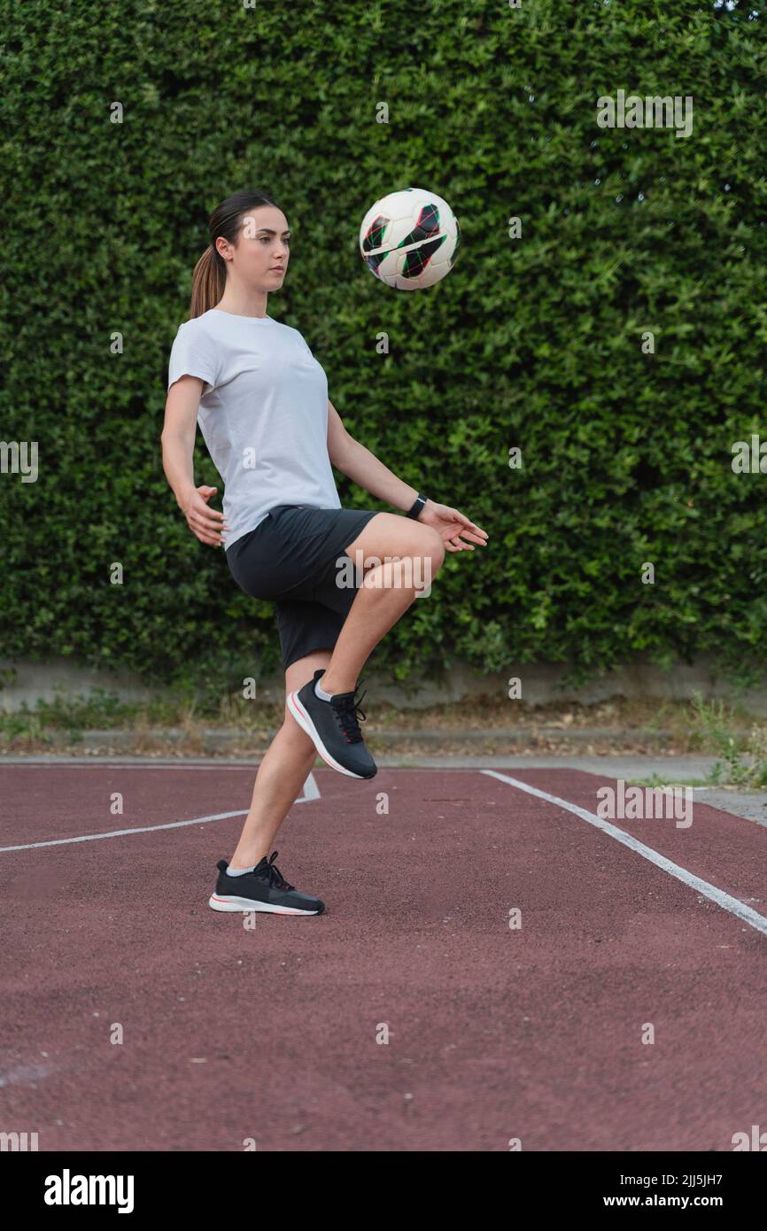 Giovane donna calcia palla di calcio con ginocchio in campo sportivo Foto Stock