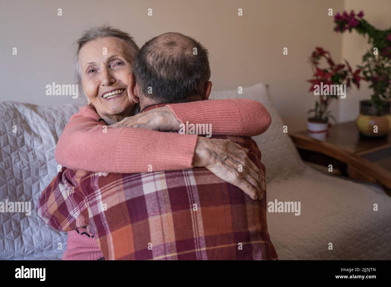 Donna anziana felice che abbraccia l'uomo maturo a casa Foto Stock