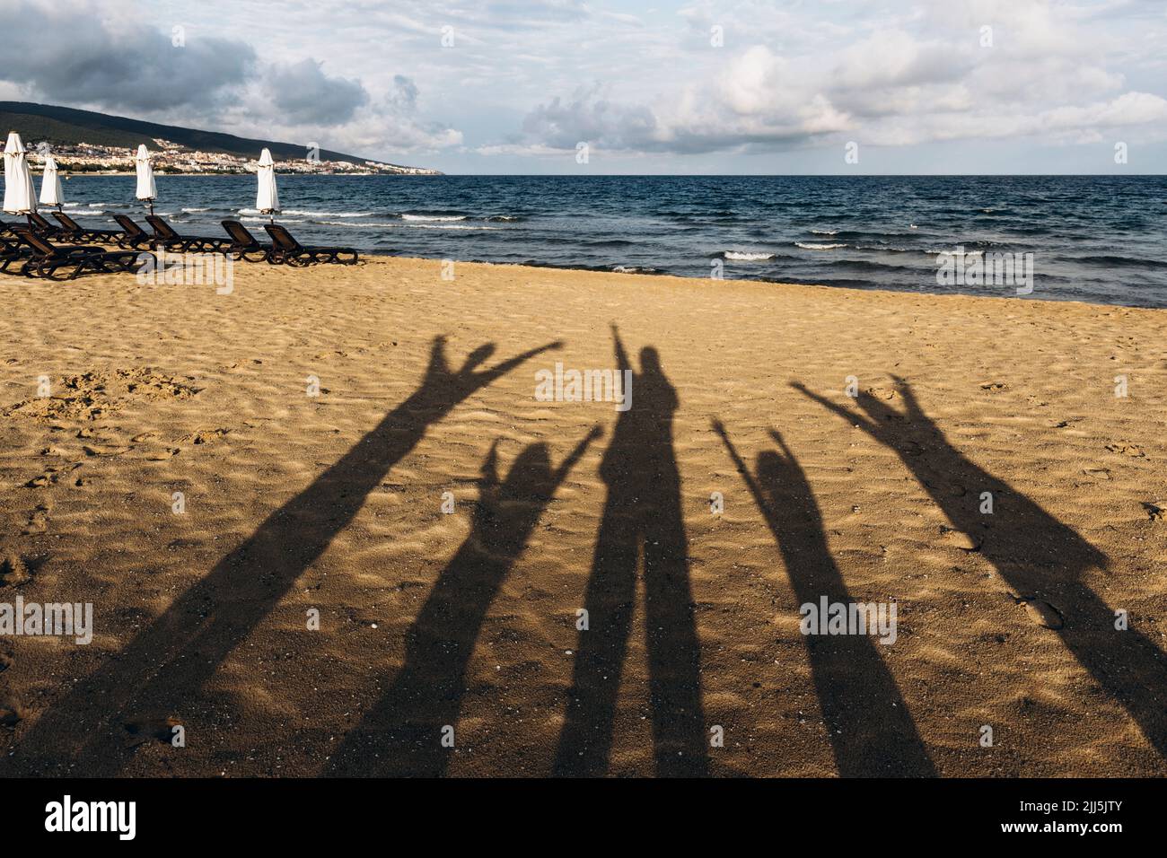 Ombre di cinque persone in piedi sulla spiaggia di sabbia con braccia sollevate Foto Stock