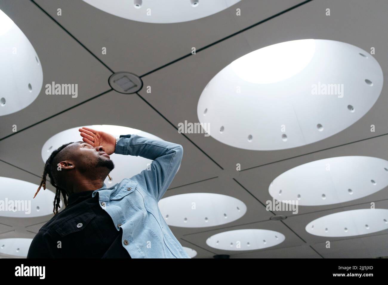 Il giovane uomo scherma gli occhi guardando il soffitto illuminato Foto Stock