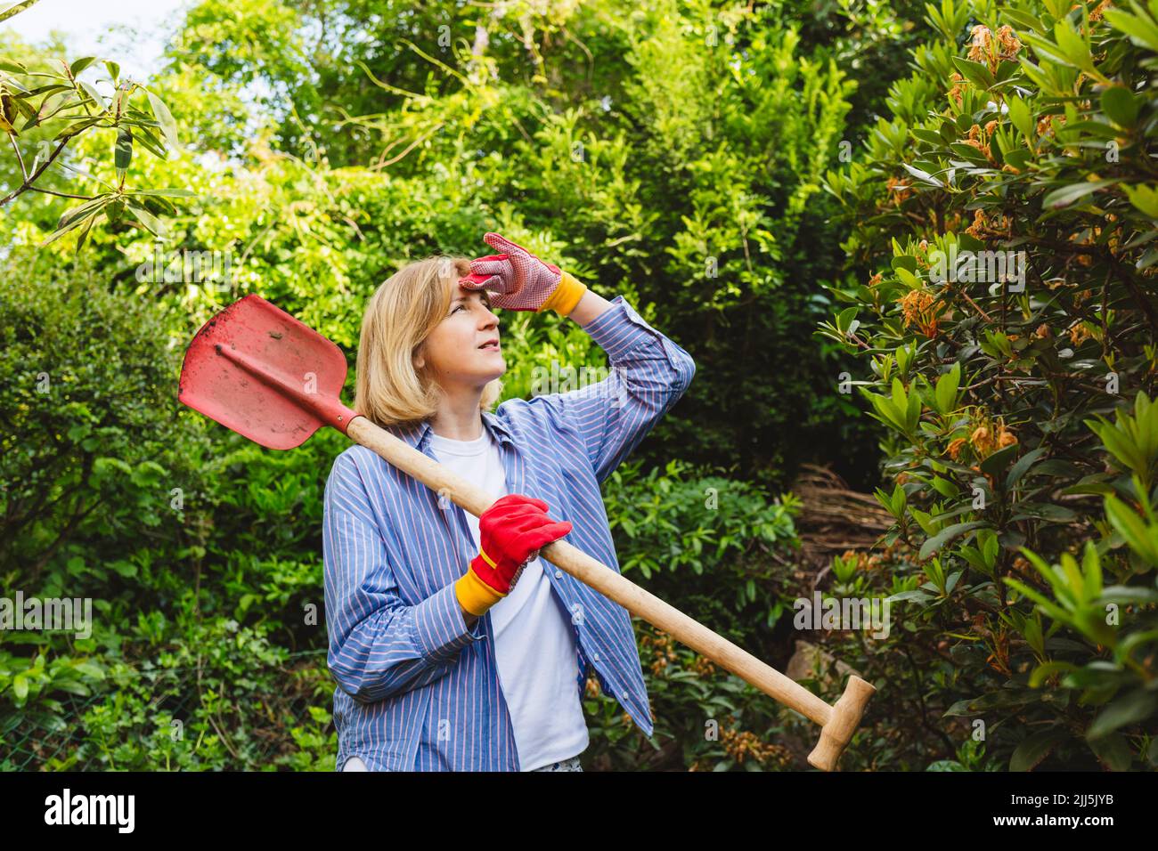 Donna scherma occhi portando pala vicino piante in giardino Foto Stock
