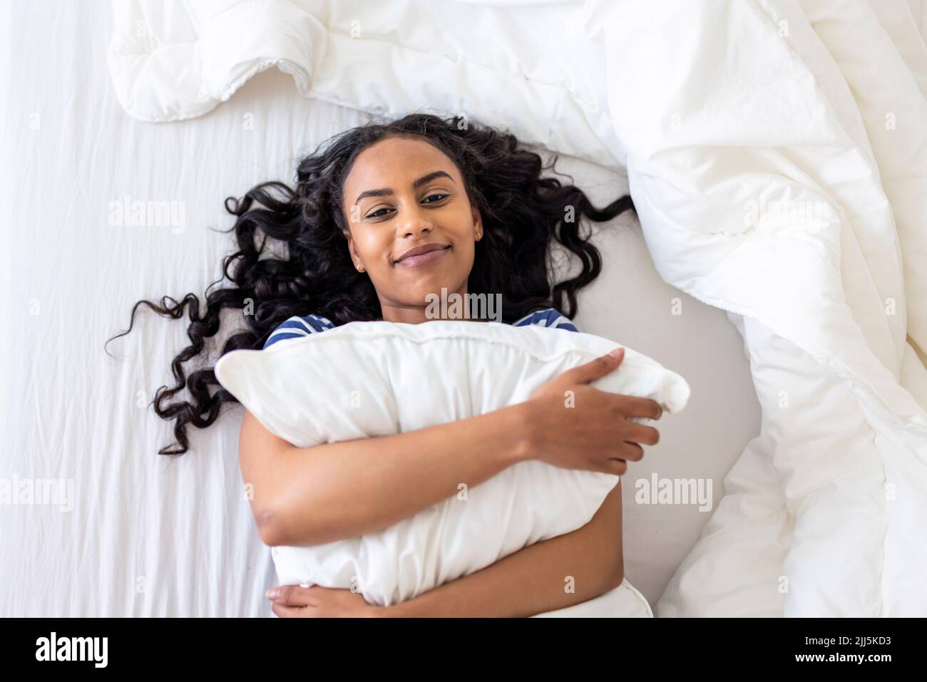 Donna felice che abbraccia il cuscino sul letto a casa Foto Stock