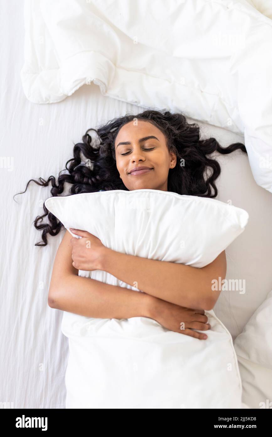 Donna felice con occhi chiusi abbracciando cuscino sul letto in camera da letto Foto Stock