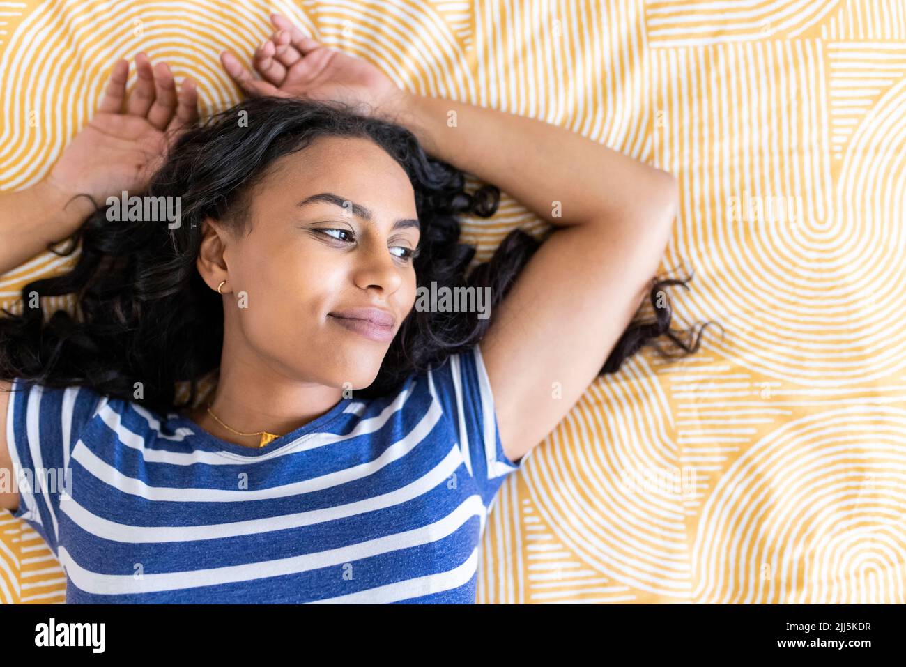 Donna pensierosa con le braccia sollevate giacenti sul letto di casa Foto Stock