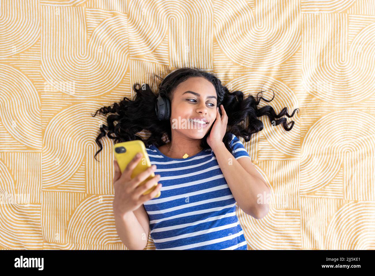 Giovane donna con smartphone che ascolta musica in camera da letto Foto Stock