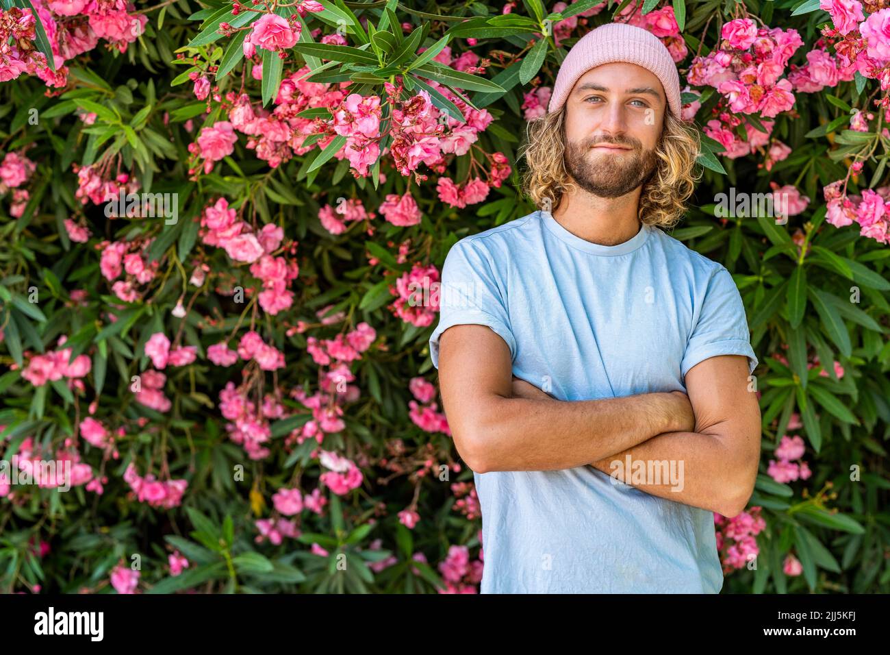 Uomo sorridente in piedi con le braccia incrociate di fronte alla pianta da fiore Foto Stock