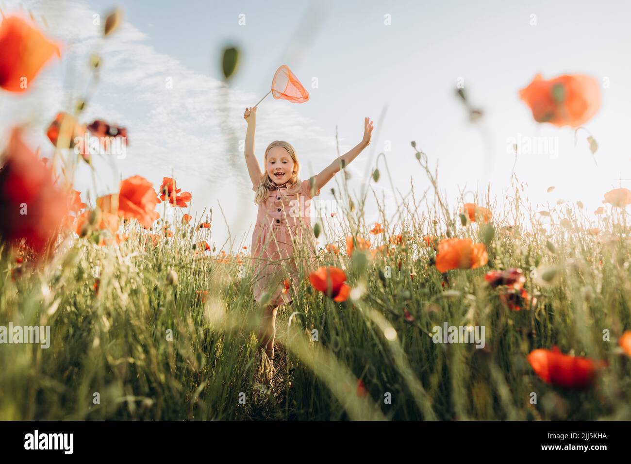 Ragazza felice inseguimento farfalle in campo papavero Foto Stock