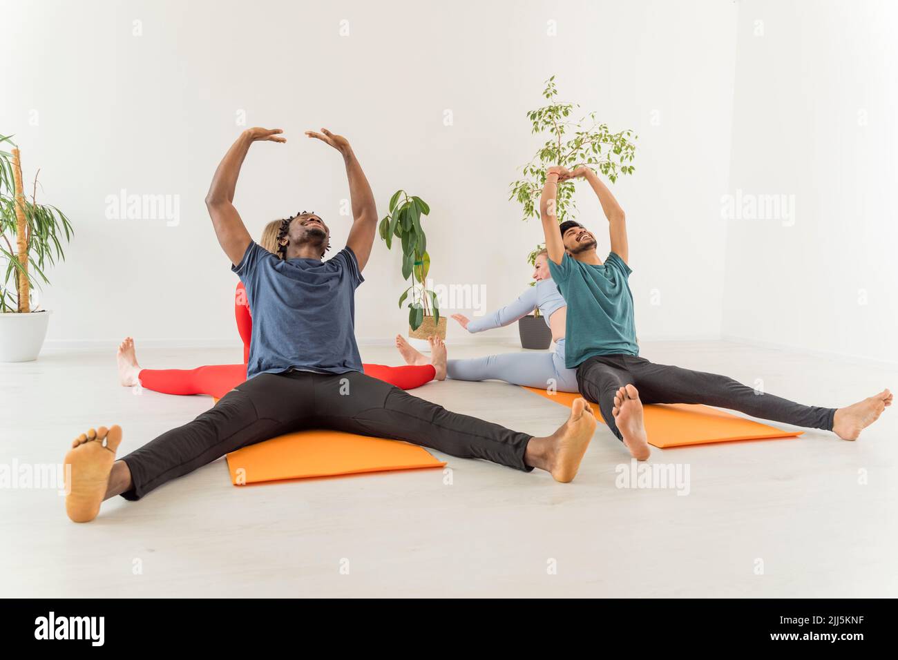 Le coppie multirazziali che praticano lo stretching esercitano insieme nello studio yoga Foto Stock