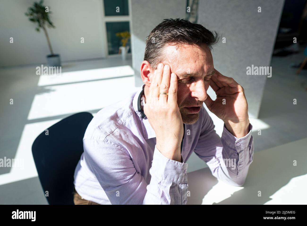 Un uomo d'affari frustrato con la testa in mano seduta in ufficio Foto Stock