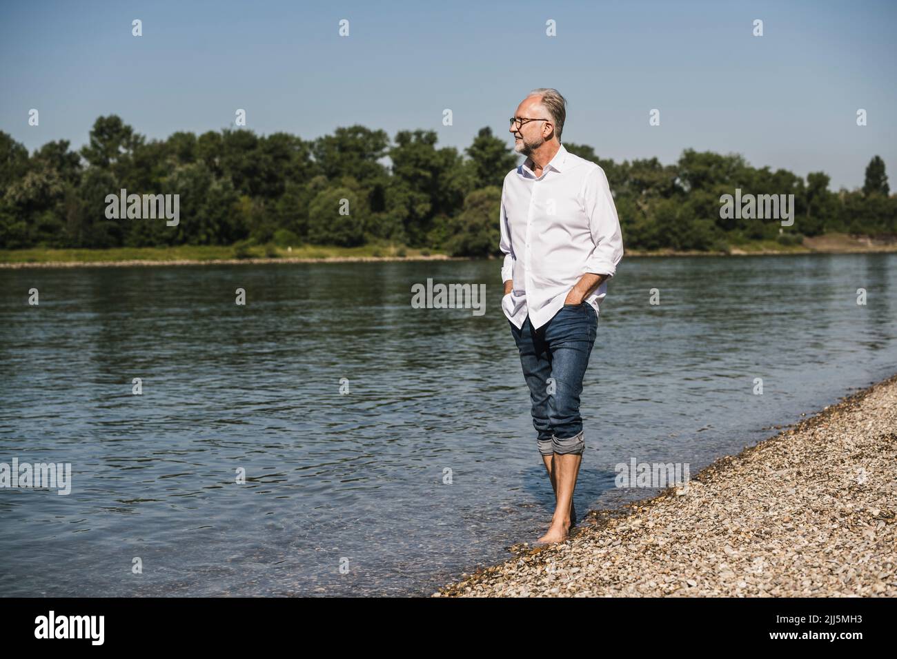 Uomo anziano con le mani in tasca che cammina sul lungofiume Foto Stock