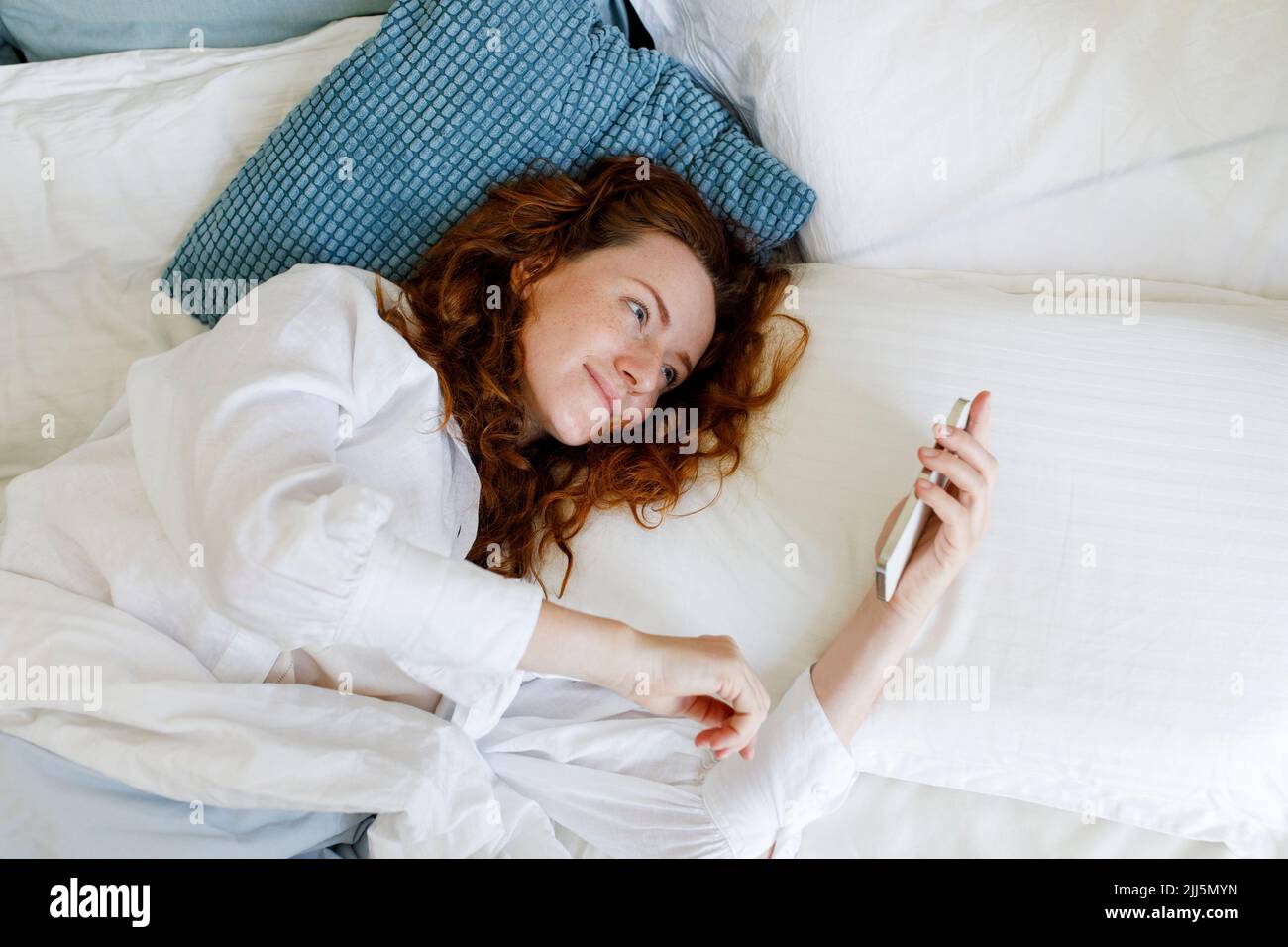 Donna con capelli marroni utilizzando smartphone sdraiato sul letto Foto Stock