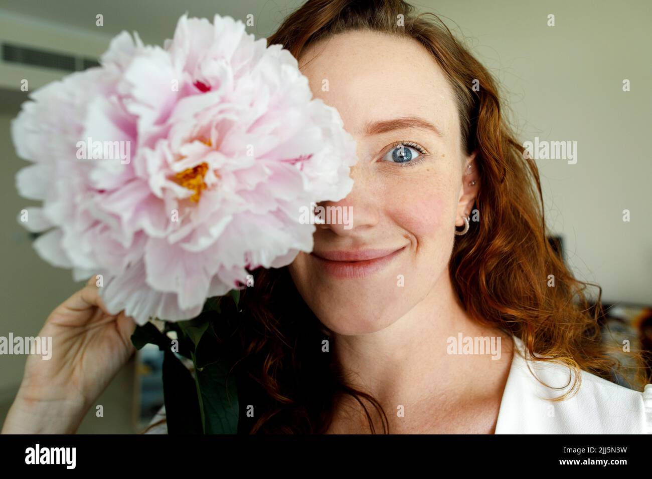 Donna sorridente che tiene il fiore davanti all'occhio Foto Stock