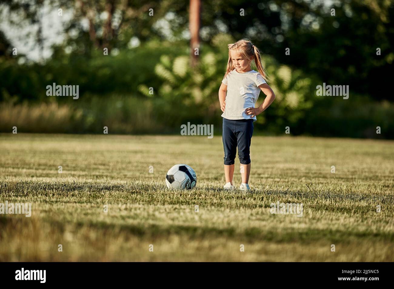 Ragazza in piedi con mano su anca da calcio palla a campo sportivo Foto Stock