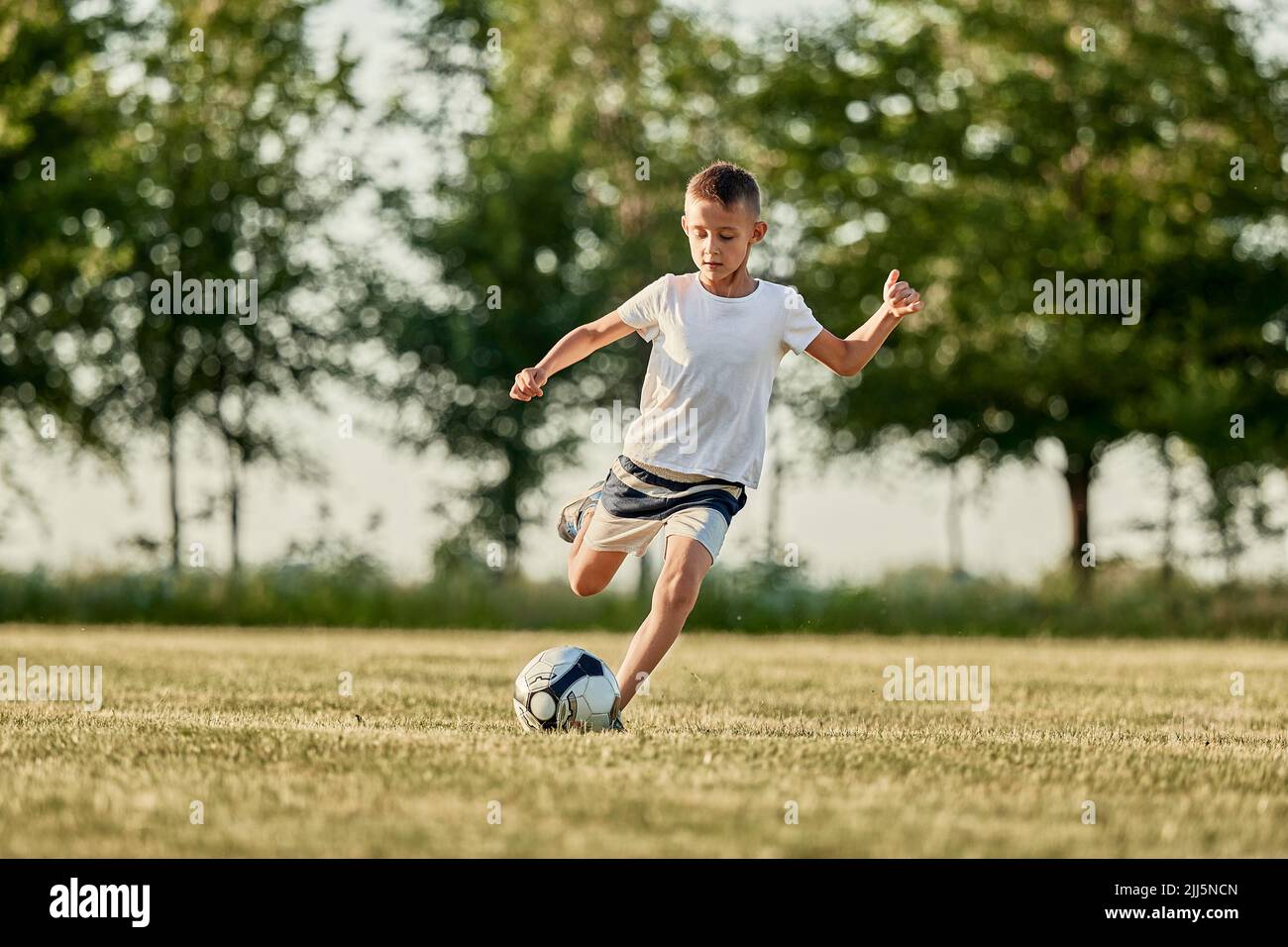 Il ragazzo calcia la palla di calcio al campo sportivo in giorno di sole Foto Stock