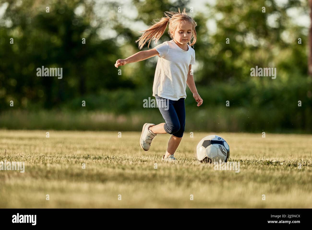 Ragazza bionda che gioca a calcio il giorno di sole Foto Stock