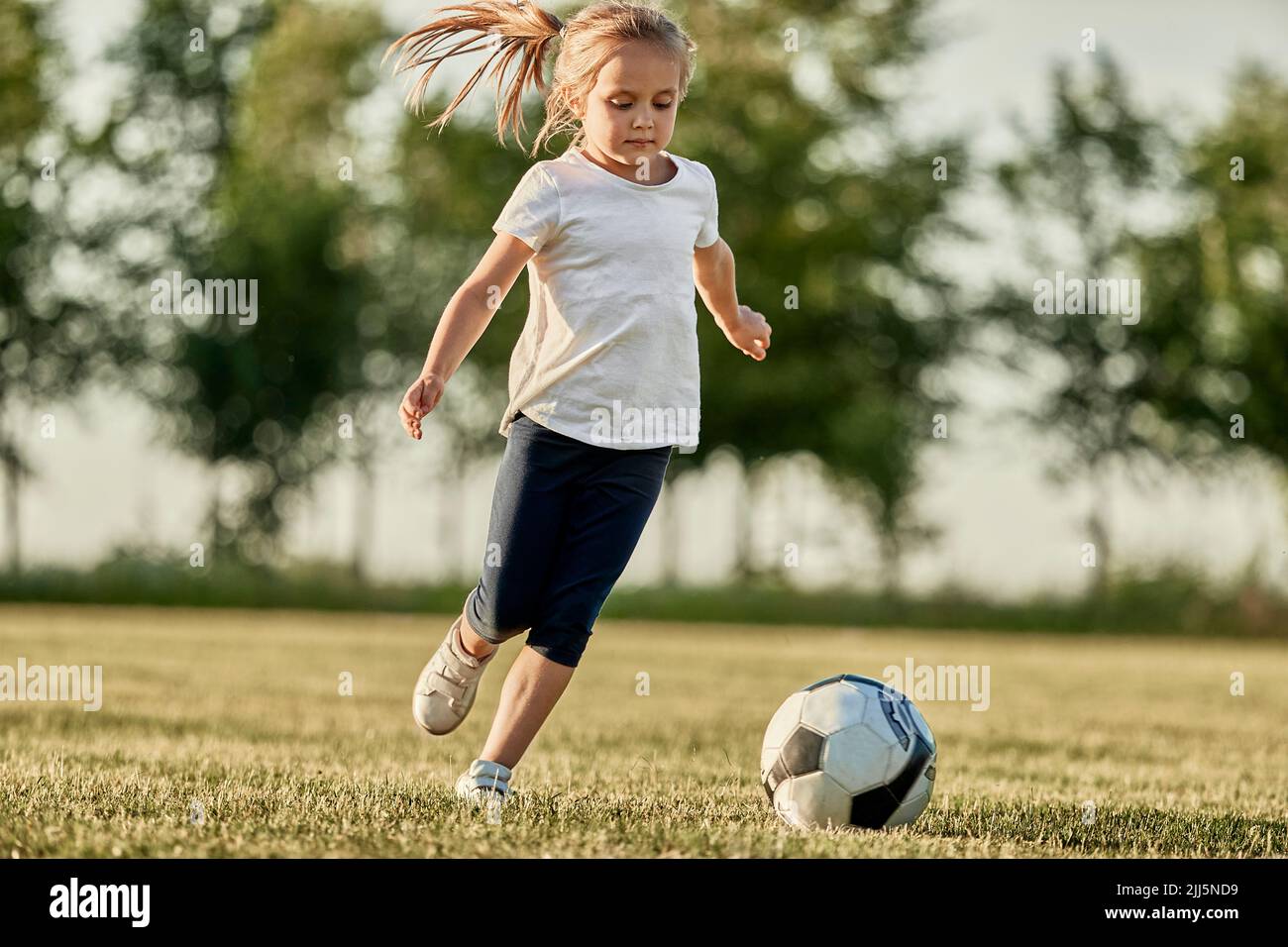 Ragazza bionda che gioca a calcio in campo sportivo il giorno di sole Foto Stock