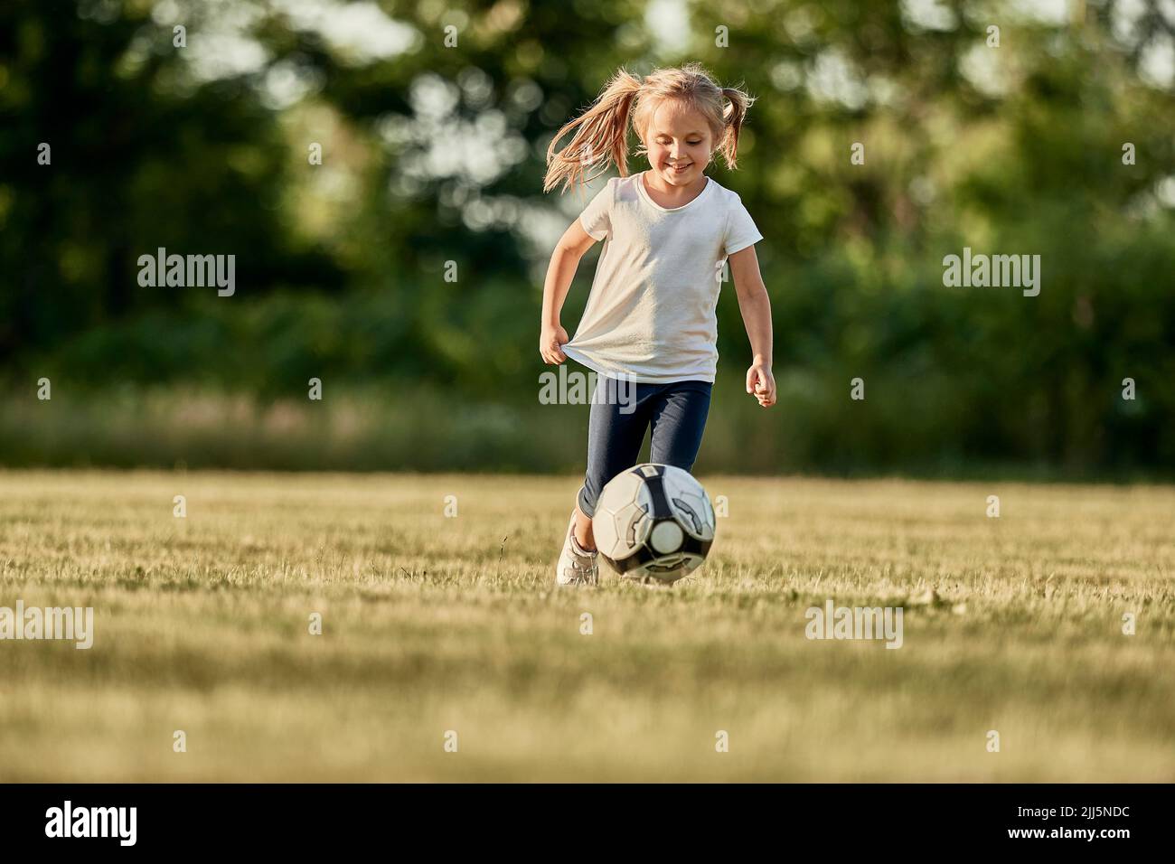 Felice ragazza bionda che gioca a calcio in campo sportivo Foto Stock