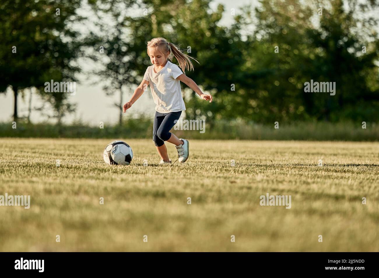 Ragazza che gioca a calcio in campo sportivo in giornata di sole Foto Stock