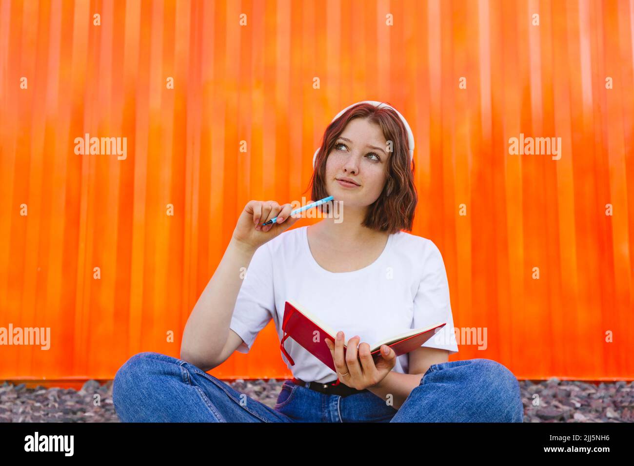 Ragazza pensierosa adolescente con il taccuino seduto davanti al contenitore arancione del carico Foto Stock