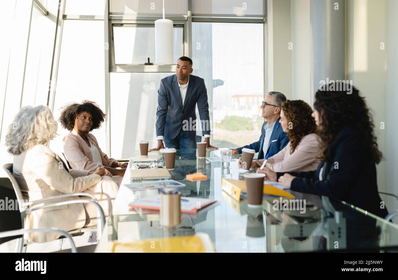 Uomo d'affari che guarda i colleghi che condividono idee durante una riunione in ufficio Foto Stock