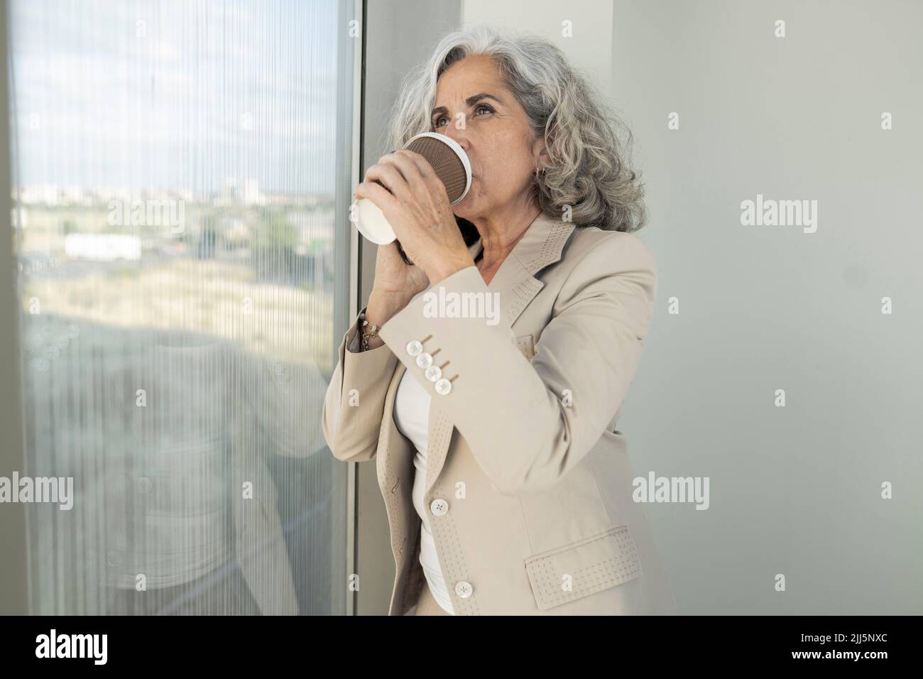 Donna d'affari che beve caffè da tazza usa e getta in ufficio Foto Stock
