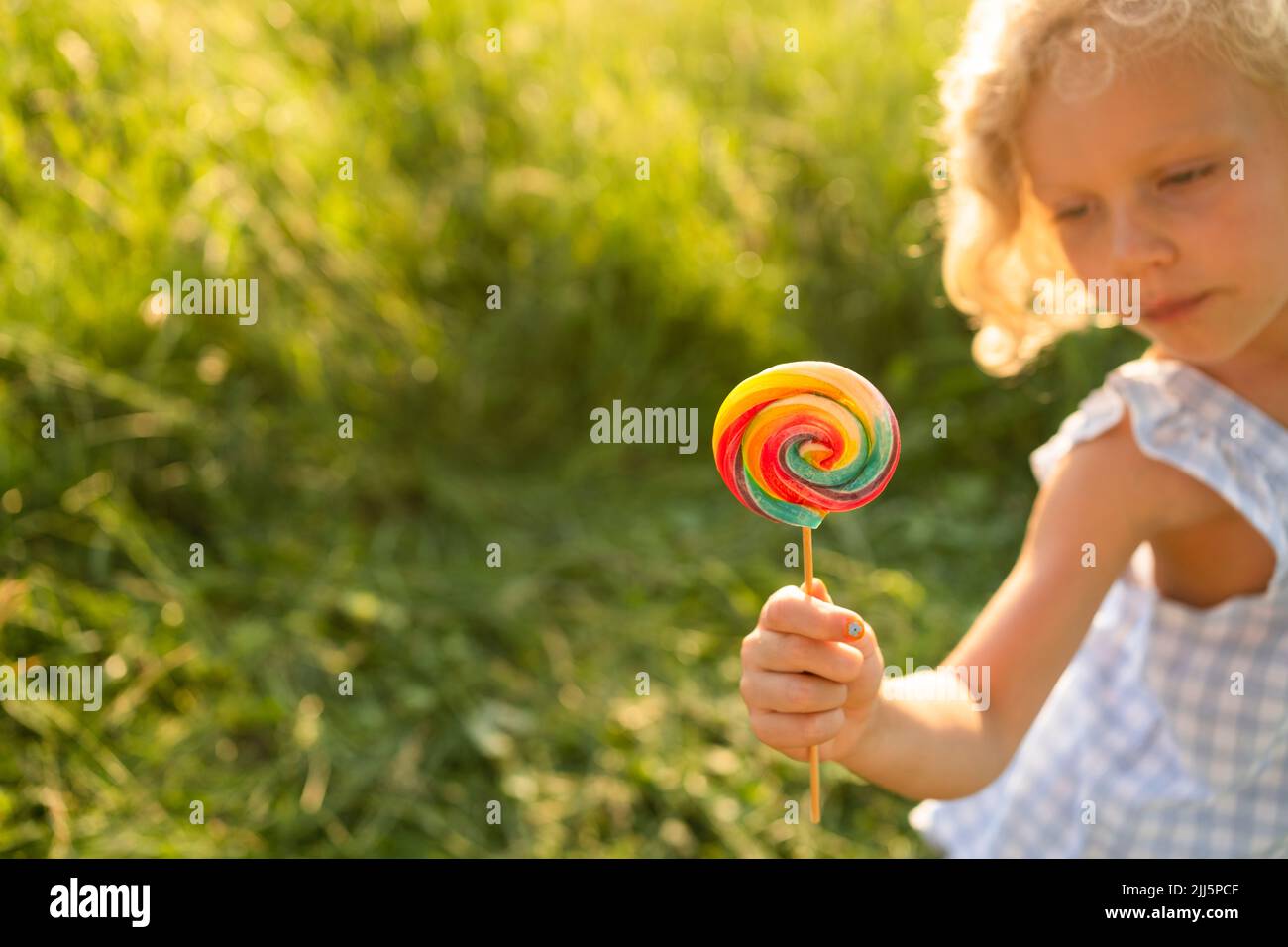 Ragazza che tiene arcobaleno lolllipop in giorno di sole Foto Stock