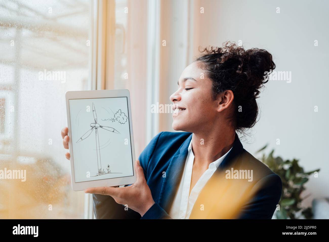 Felice donna d'affari che tiene un tablet PC con disegno a turbina eolica in ufficio Foto Stock Felice donna d'affari che tiene un tablet PC con disegno a turbina eolica in ufficio Foto Stock