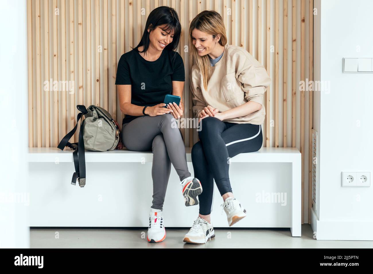 Donna sorridente che mostra lo smartphone ad un amico dopo una sessione di yoga nel centro benessere Foto Stock