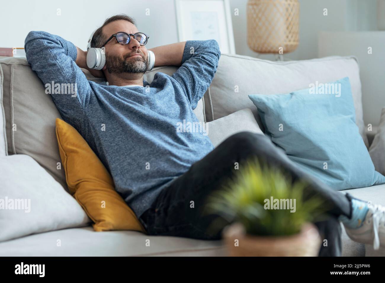 Uomo sorridente che ascolta la musica con le cuffie rilassarsi sul divano a casa Foto Stock