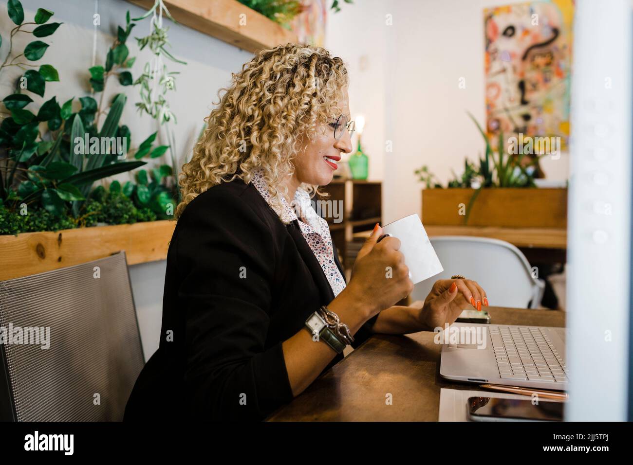 Donna d'affari con tazza di caffè utilizzando un computer portatile in ufficio Foto Stock