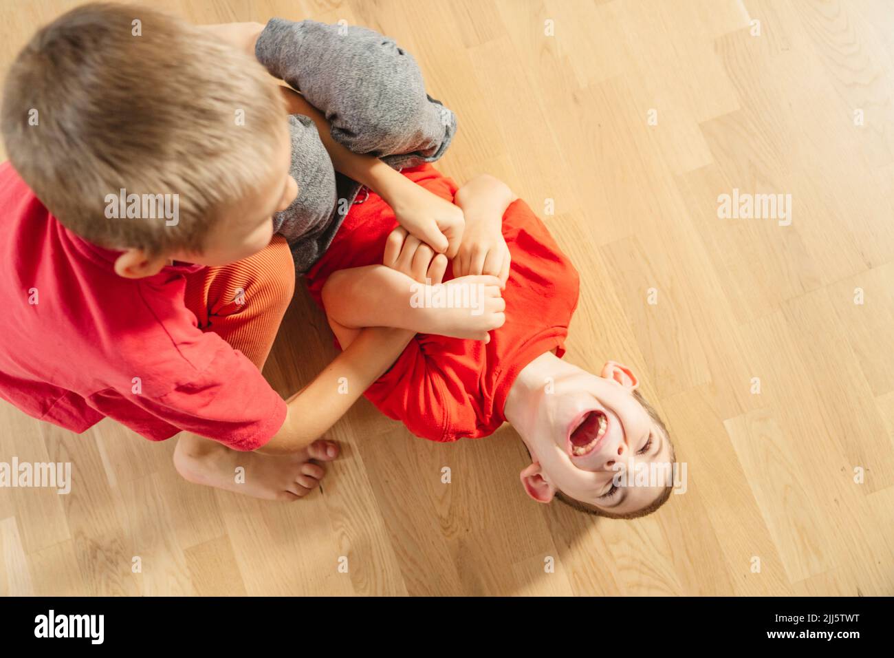 Ragazzo solletico fratello giacente sul pavimento a casa Foto Stock