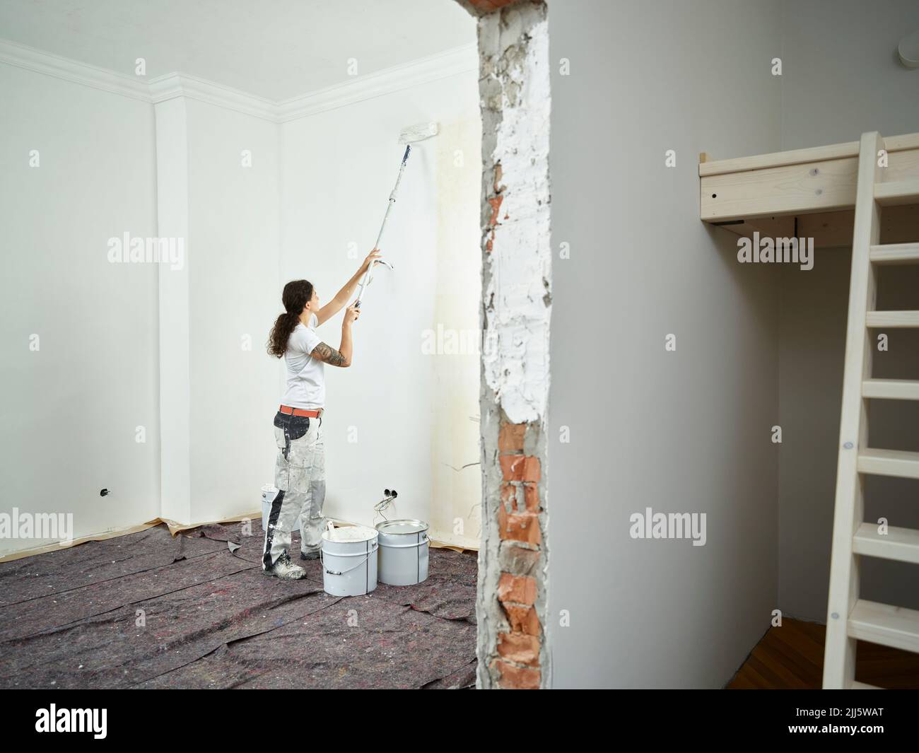 Pittore che fa pittura finale con rullo di vernice in appartamento Foto Stock