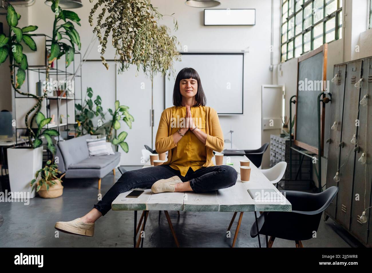 Donna d'affari che medita con le mani afferrate sulla scrivania sul posto di lavoro Foto Stock