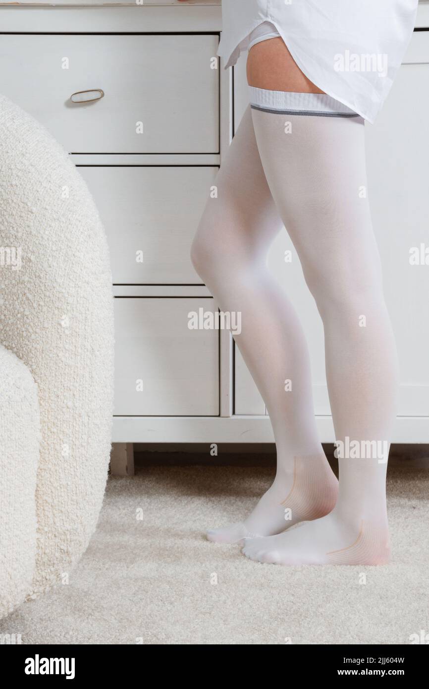 Calze bianche. Belle lunghe gambe femminili in calze. Ragazza che mette su calze a casa in una stanza bianca. Prevenzione delle vene varicose. Corpo donna dentro Foto Stock