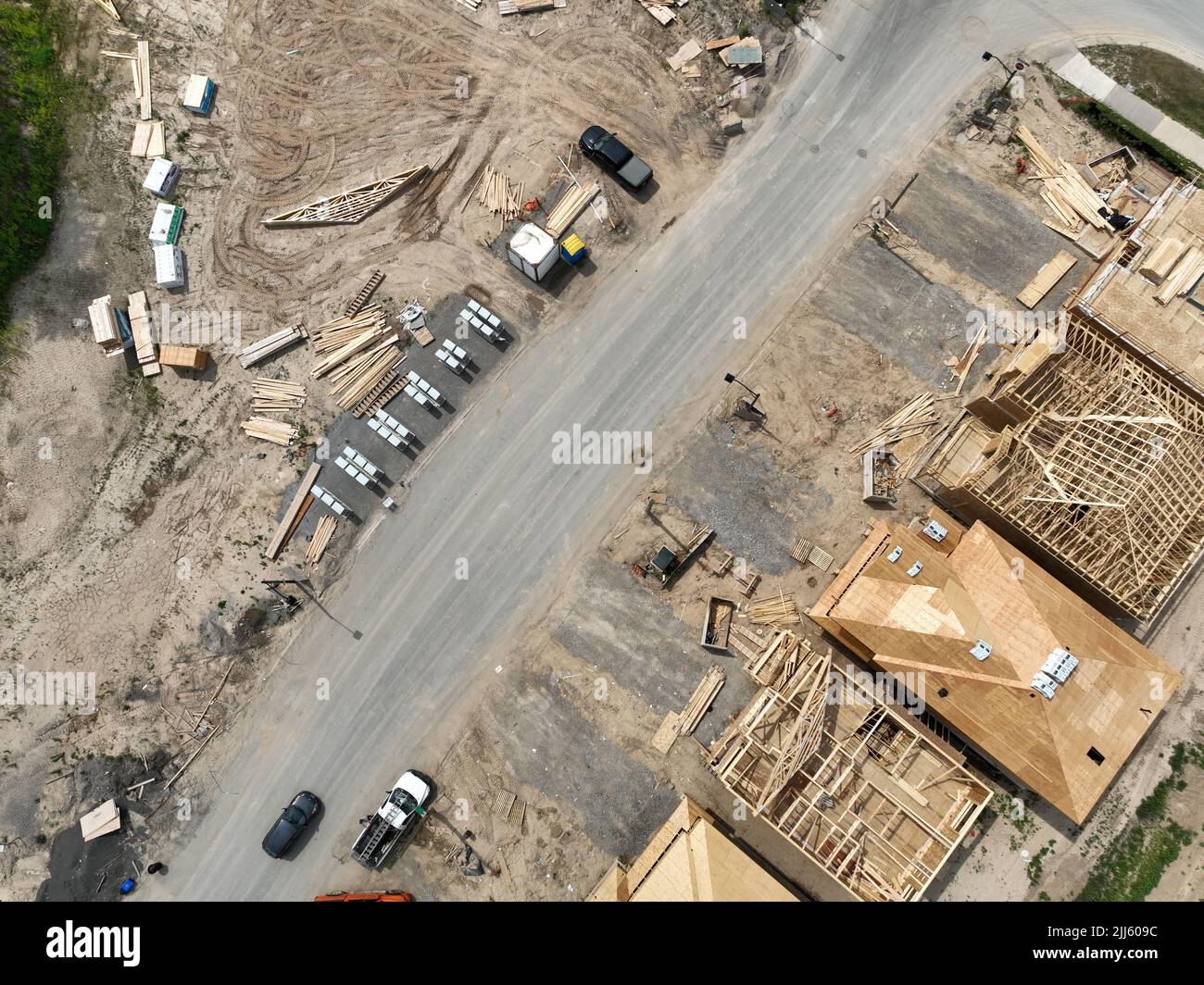 Una diagonale vista aerea direttamente sopra un quartiere, strada residenziale in costruzione come le case sono in costruzione. Materiale e forniture per tetti. Foto Stock