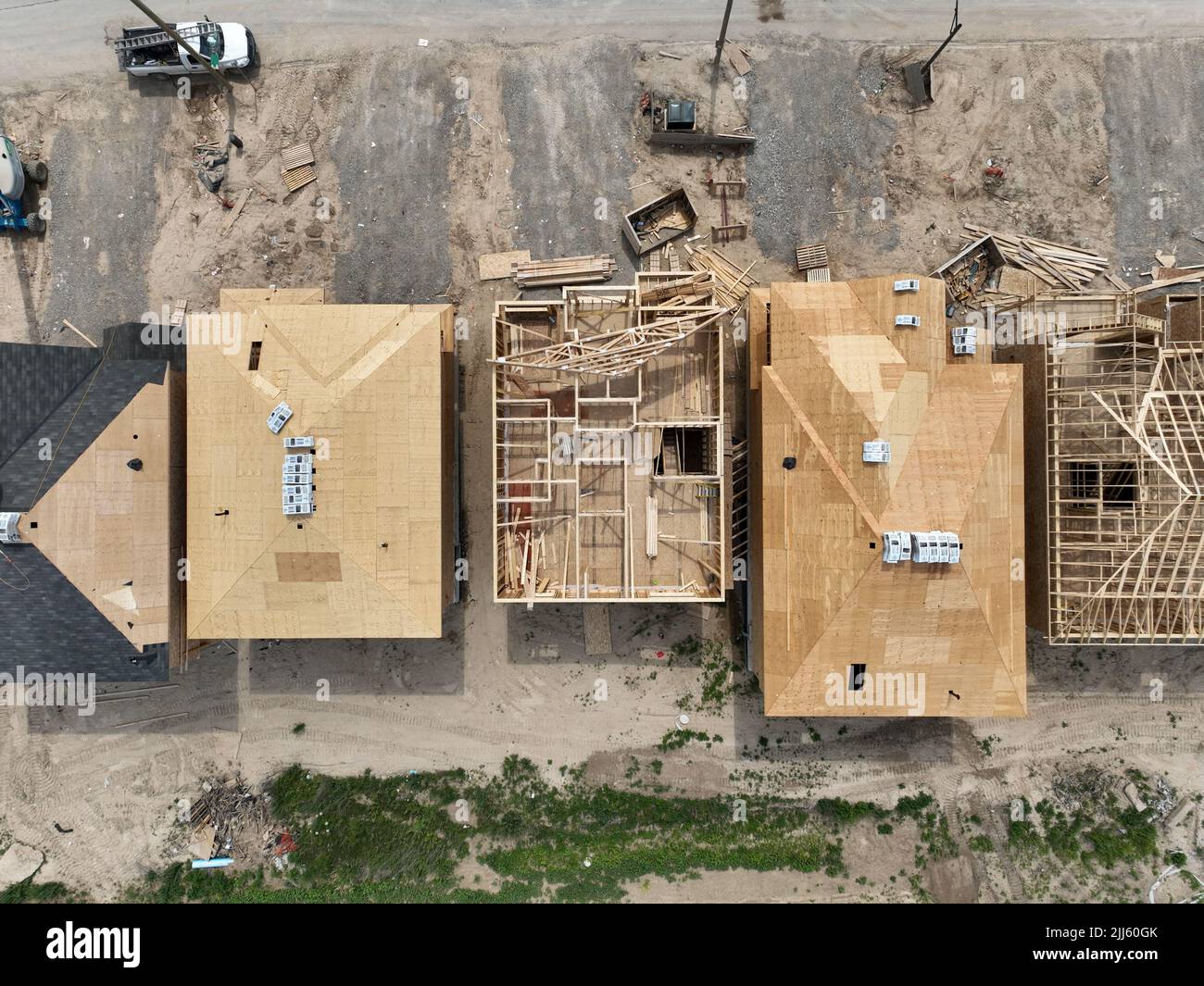 Una vista aerea sopra una fila di nuove case in costruzione. Installazione di strutture in legno e tetti vista in corso direttamente dall'alto. Foto Stock
