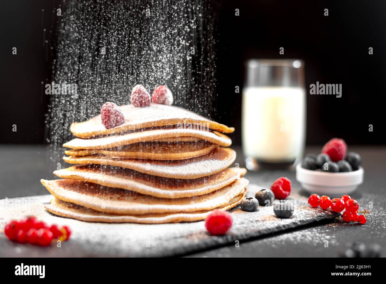 Grandi pancake americani su sfondo scuro. Colazione europea. Lo chef cosparge le frittelle con lo zucchero a velo su sfondo nero. Foto Stock