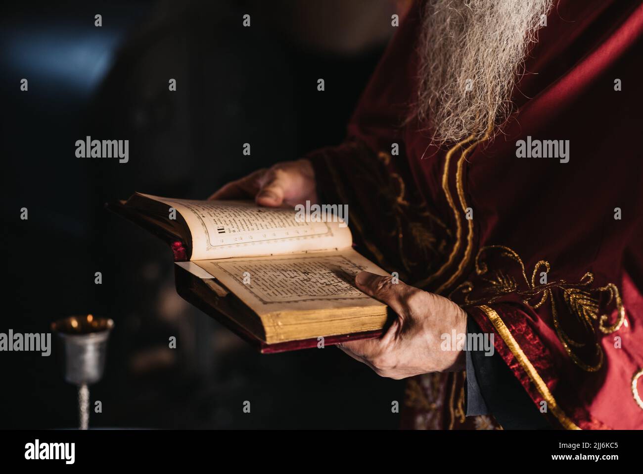 Un primo colpo di un vecchio prete saggio con una barba lunga che legge la bibbia Foto Stock