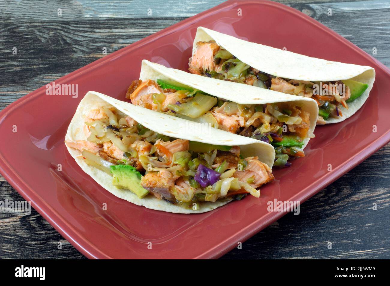 Tre tacos di salmone con avocado e verdure su piatto da portata rosso Foto Stock