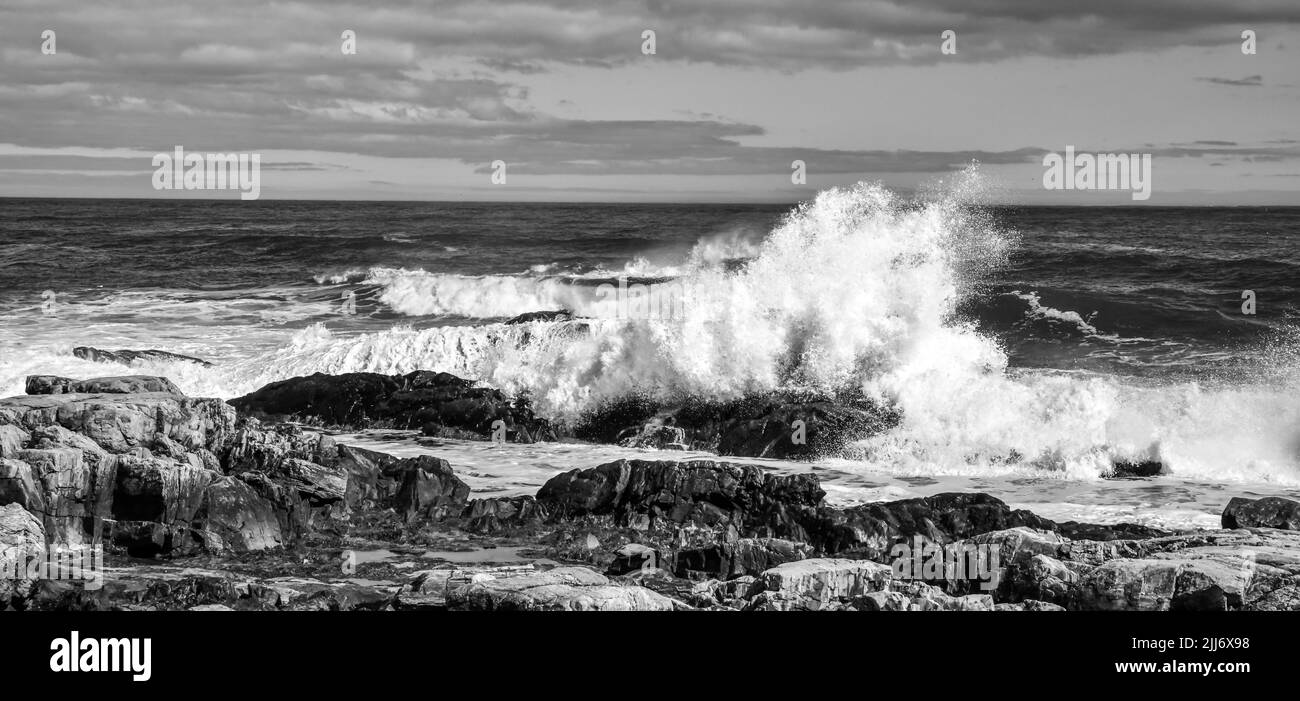 vista panoramica delle onde che si infrangono contro le rocce sotto il cielo blu e le nuvole Foto Stock