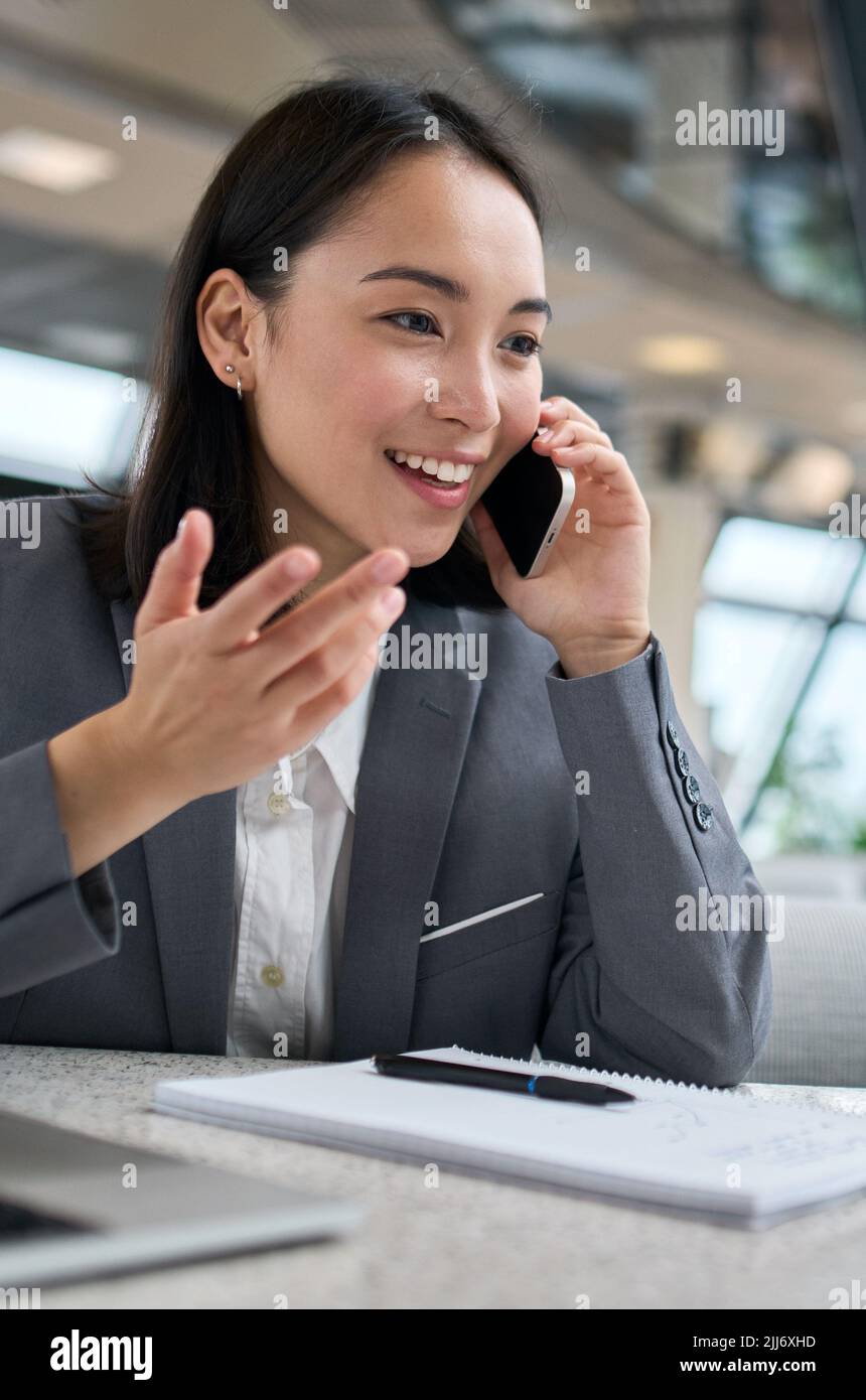 Felice giovane donna d'affari cinese che parla al telefono che lavora in ufficio. Foto Stock