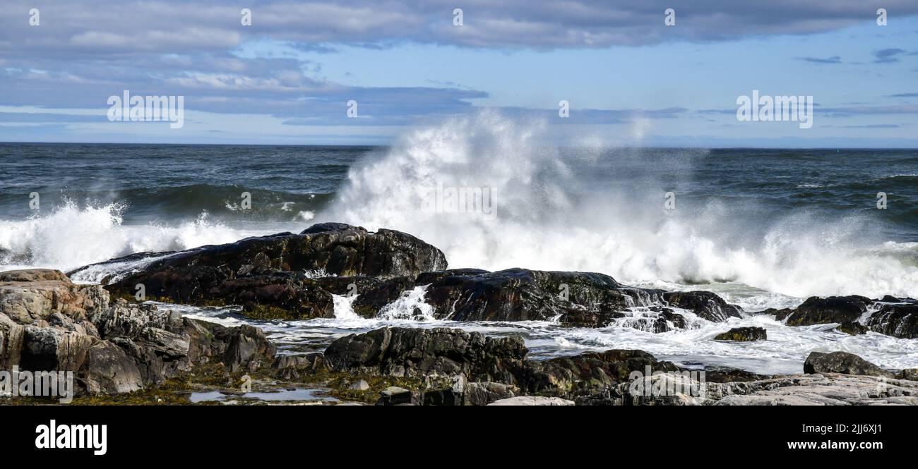 vista panoramica delle onde che si infrangono contro le rocce sotto il cielo blu e le nuvole Foto Stock