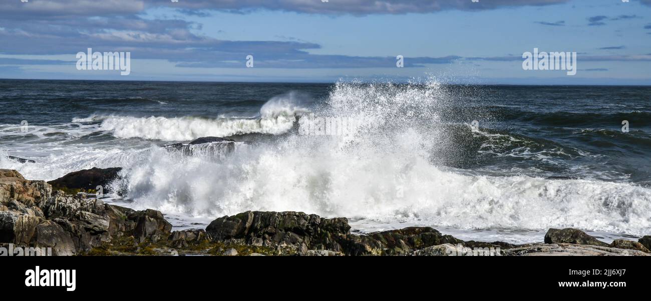 vista panoramica delle onde che si infrangono contro le rocce sotto il cielo blu e le nuvole Foto Stock